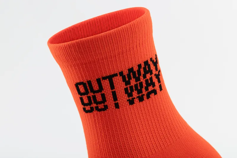 Close-up of an orange Outway crew sock with the OUTWAY wordmark knit into the cuff